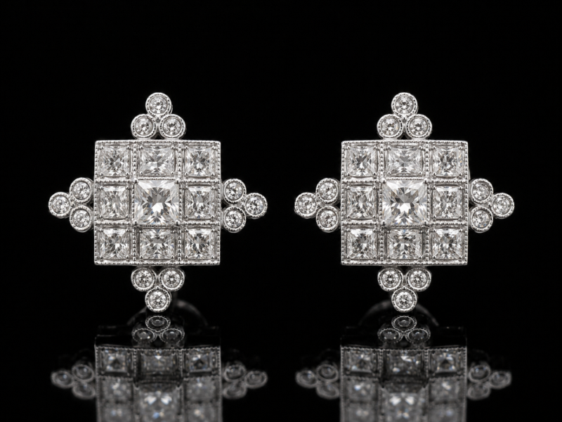 Pair of white gold diamond earrings with square diamond panels and groups of round diamond accents, reflected on a black background.
