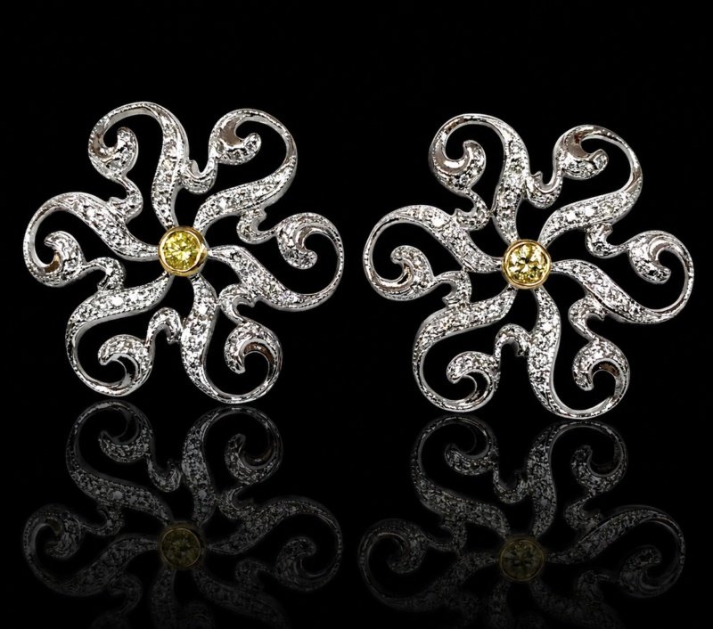 Pair of white gold flower earrings with fancy yellow diamond centers and white diamonds along curling openwork petals, reflected on a black background.