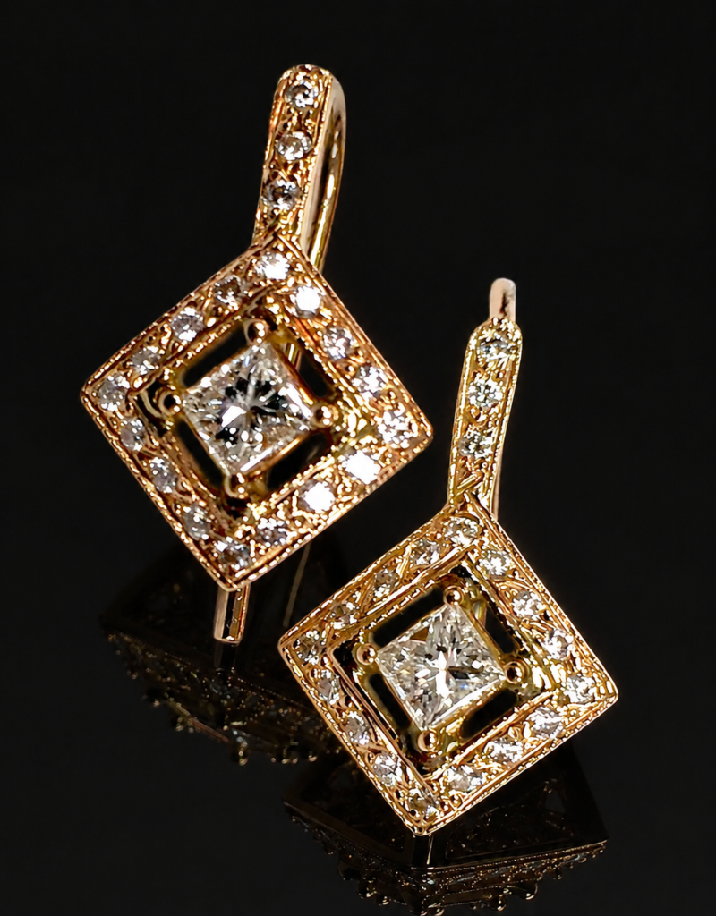 Pair of yellow gold diamond drop earrings with princess-cut centers inside tilted square diamond frames, reflected on a black background.